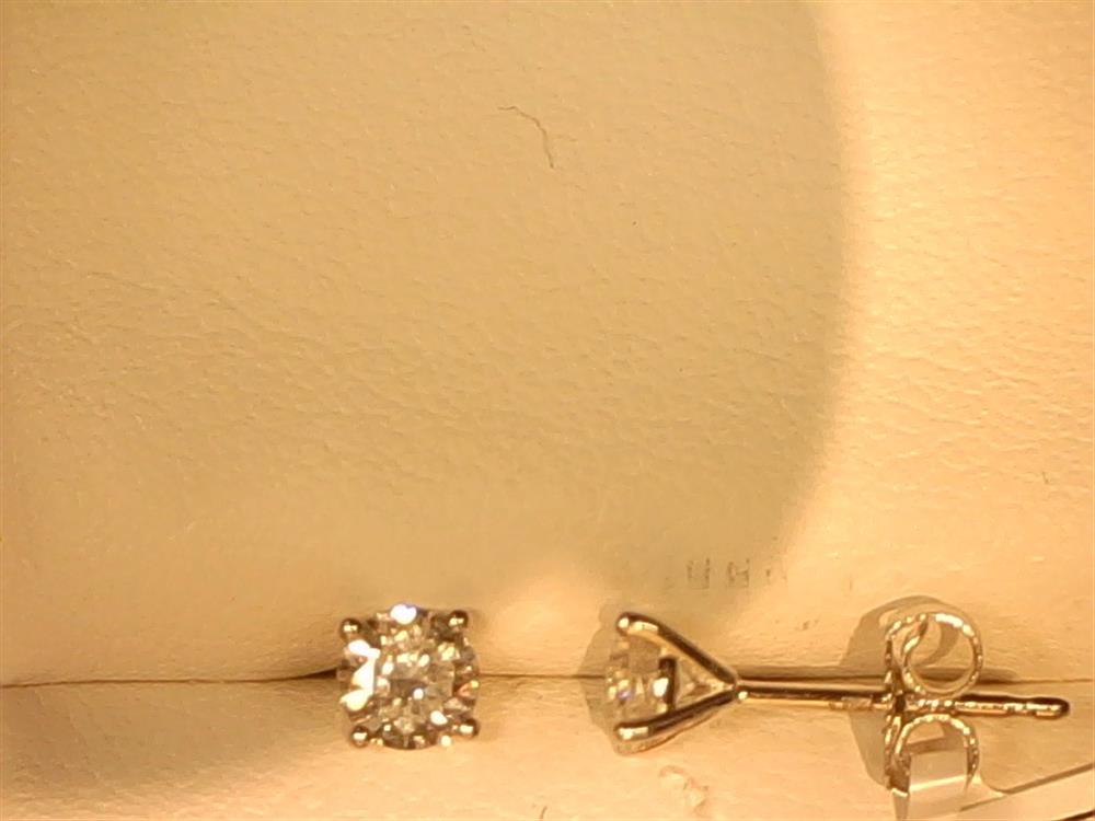 A single Simply Diamonds 14KW 1/2 CTTW Lab Grown Diamond Stud lies on its side against a beige background, showcasing its prong-set gem and butterfly clutch back.