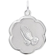 The Rembrandt Charms Praying Hands Charm in sterling silver showcases a pair of praying hands at the center, set against a textured background. The charm features a scalloped edge that creates a flower-like shape and includes a loop at the top for easy attachment to a chain or necklace.