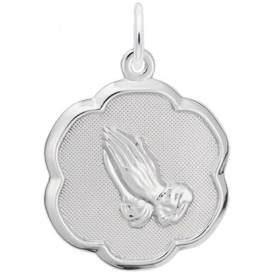 The Rembrandt Charms Praying Hands Charm in sterling silver showcases a pair of praying hands at the center, set against a textured background. The charm features a scalloped edge that creates a flower-like shape and includes a loop at the top for easy attachment to a chain or necklace.