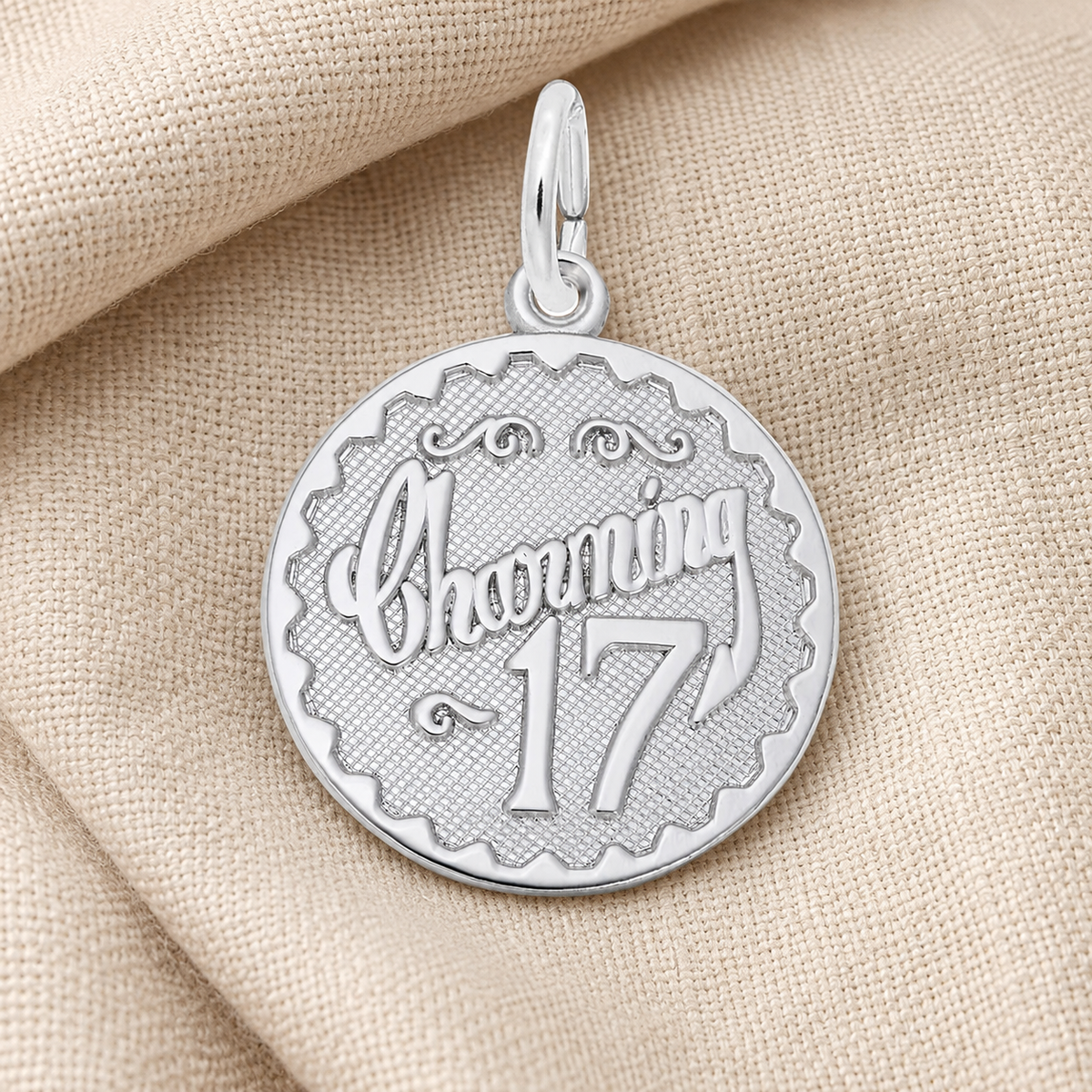 The Rembrandt Charms “Charming 17 Charm” in sterling silver features the words “Charming 17” in decorative script, elegantly displayed on a beige fabric background—a sophisticated seventeenth birthday jewelry piece and memorable milestone keepsake.