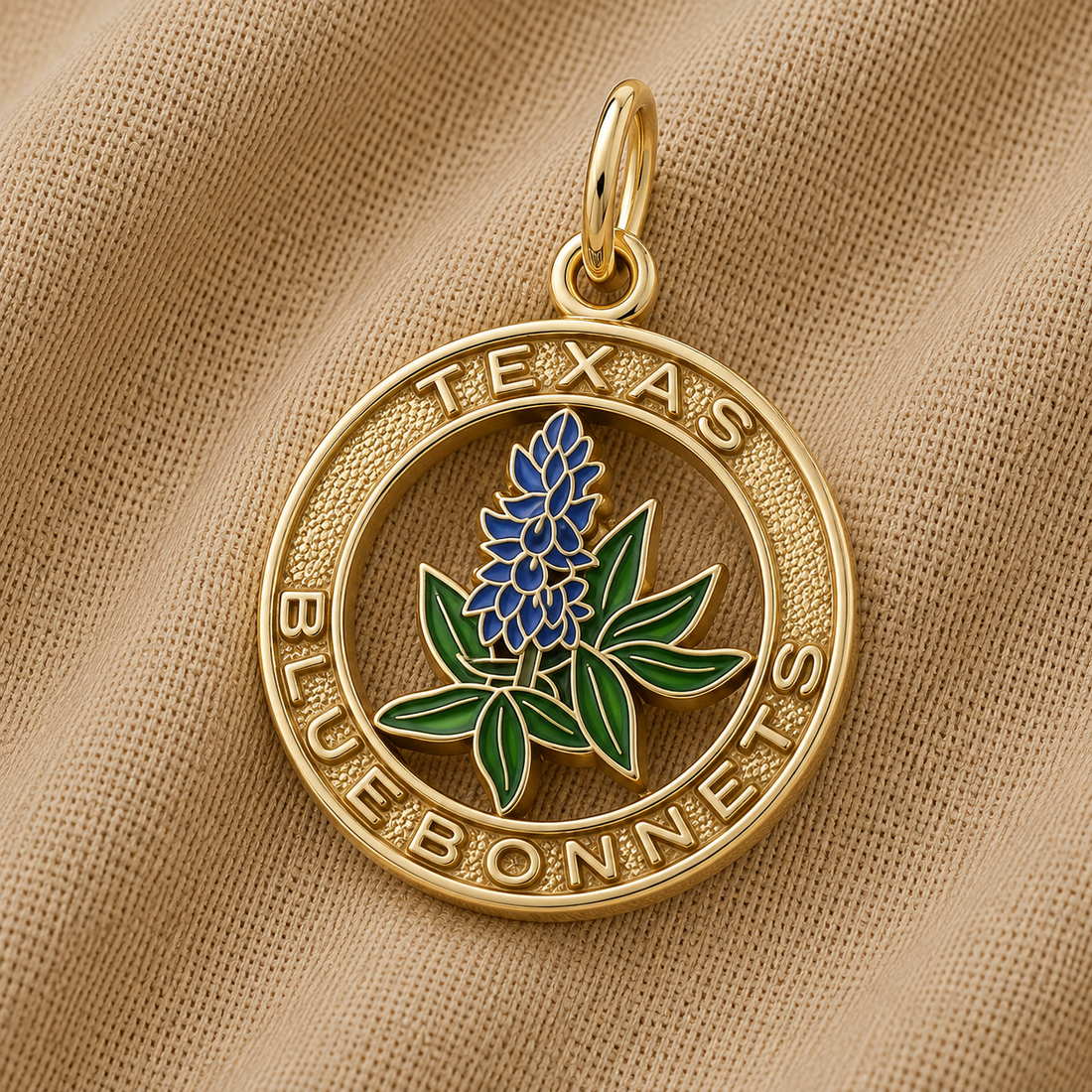 The Rembrandt Charms Texas Bluebonnets Charm - Gold Plated features a gold pendant on fabric, showcasing a bluebonnet flower at its center with “TEXAS BLUEBONNETS” engraved around the edge in capital letters. This elegant piece beautifully captures the natural beauty and state pride of Texas, making it a meaningful addition to any jewelry collection.
