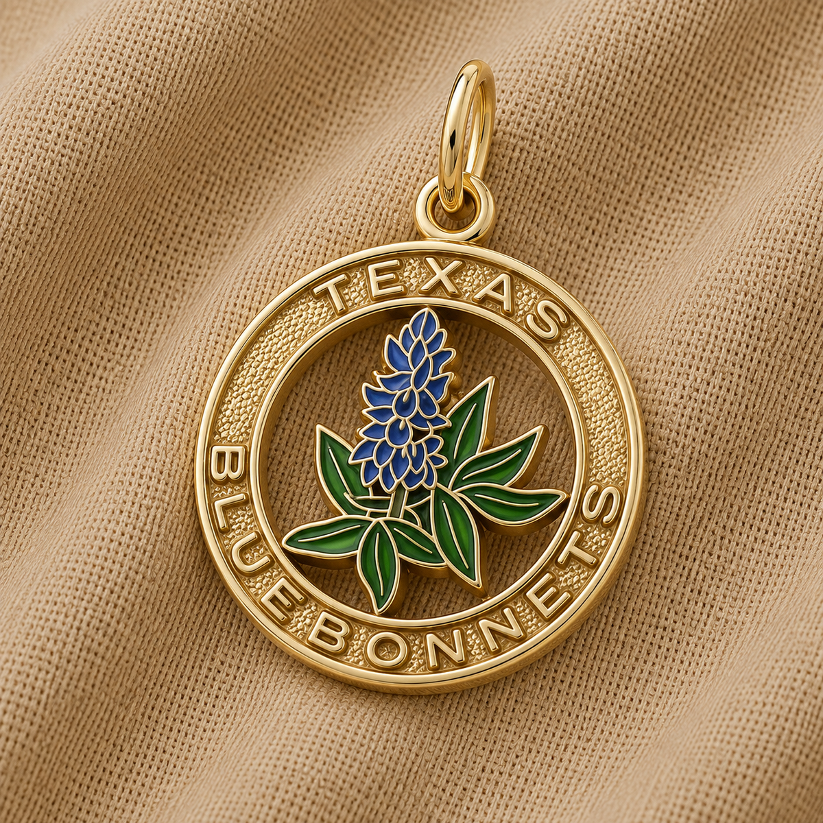 The Rembrandt Charms Texas Bluebonnets Charm - Gold Plated features a gold pendant on fabric, showcasing a bluebonnet flower at its center with “TEXAS BLUEBONNETS” engraved around the edge in capital letters. This elegant piece beautifully captures the natural beauty and state pride of Texas, making it a meaningful addition to any jewelry collection.