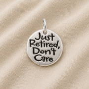 The Rembrandt Charms Just Retired disc sterling silver charm, featuring the inscription “Just Retired, Don’t Care,” is displayed against a beige fabric background—an ideal and unique addition to any charm bracelet or a thoughtful retirement gift.