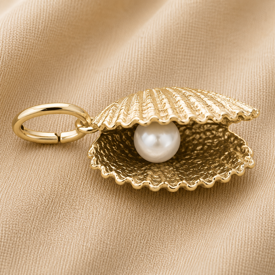 The Shell With Pearl Charm- Gold Plated by Rembrandt Charms, featuring a gold-plated seashell design with a lustrous white pearl inside, is displayed on a beige fabric background, capturing the elegance of ocean-inspired jewelry.