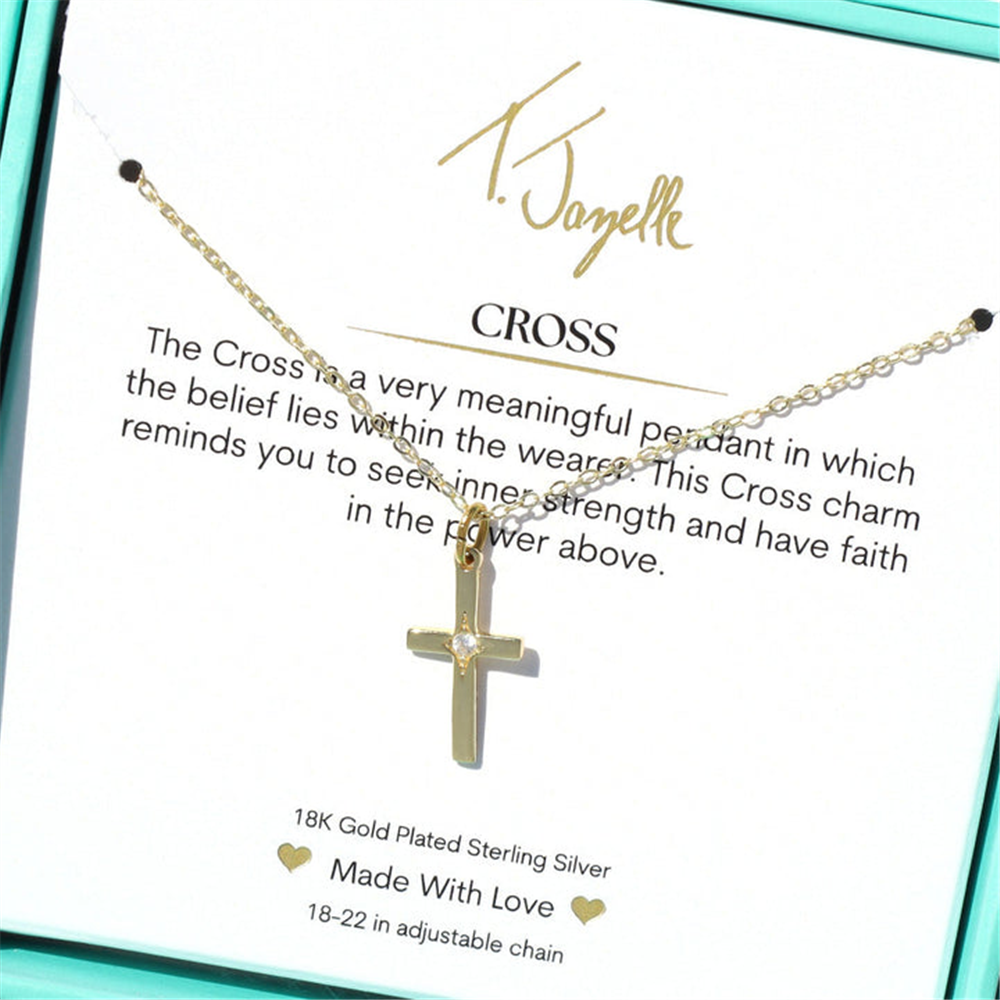 The T Jazelle Cross CZ Gold Charm Necklace features a 14k gold plated sterling silver cross with a CZ gemstone on an adjustable chain, displayed on a card with a motivational faith and strength message.