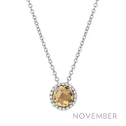 The "November Birthstone Necklace" by Lafonn showcases a stunning round yellow gemstone, symbolizing the November birthstone, encircled by sparkling clear stones. This elegant pendant is suspended from a delicate silver chain. The word "November" is highlighted in purple text at the bottom right corner of the image.