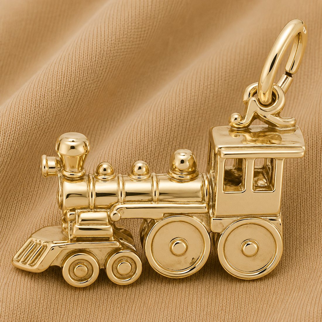 A Rembrandt Charms Train Engine Charm- Gold Plated with a large loop rests on a tan fabric background.