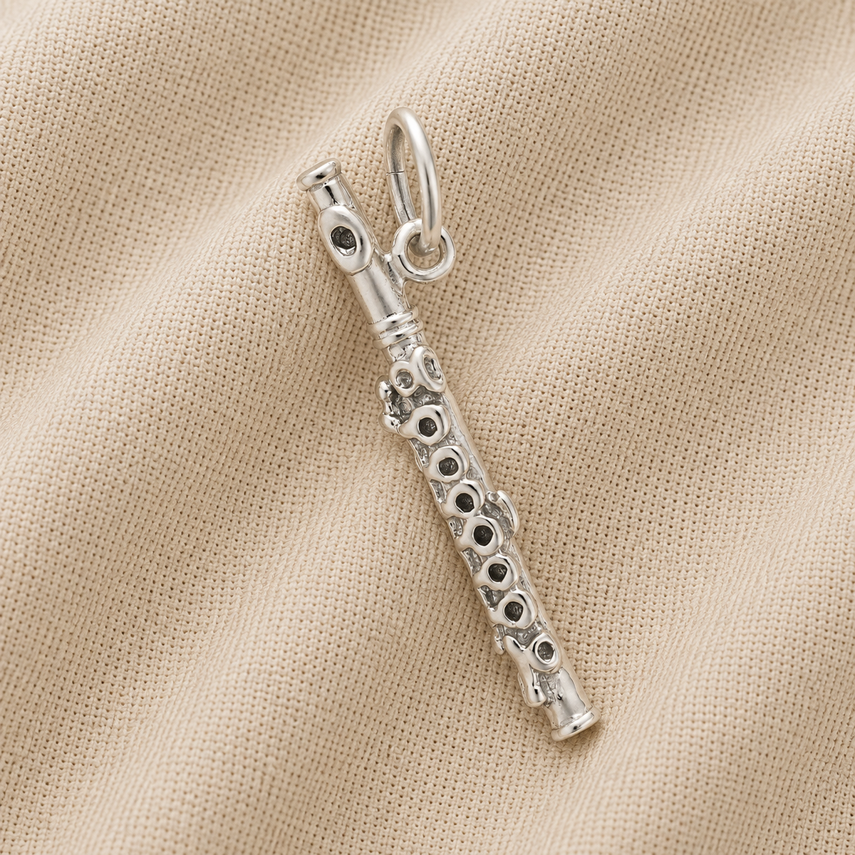 The Rembrandt Charms Piccolo - Sterling Silver Charm, featuring detailed key accents reminiscent of a musical instrument, is displayed resting on beige fabric with a subtle ribbed texture.