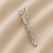 The Rembrandt Charms Piccolo - Sterling Silver Charm, featuring detailed key accents reminiscent of a musical instrument, is displayed resting on beige fabric with a subtle ribbed texture.