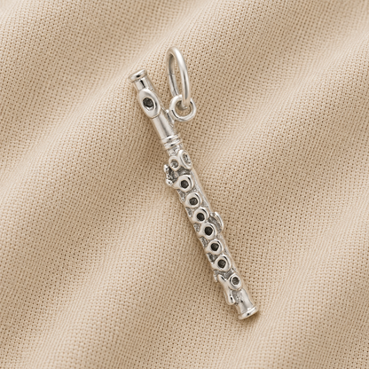 The Rembrandt Charms Piccolo - Sterling Silver Charm, featuring detailed key accents reminiscent of a musical instrument, is displayed resting on beige fabric with a subtle ribbed texture.
