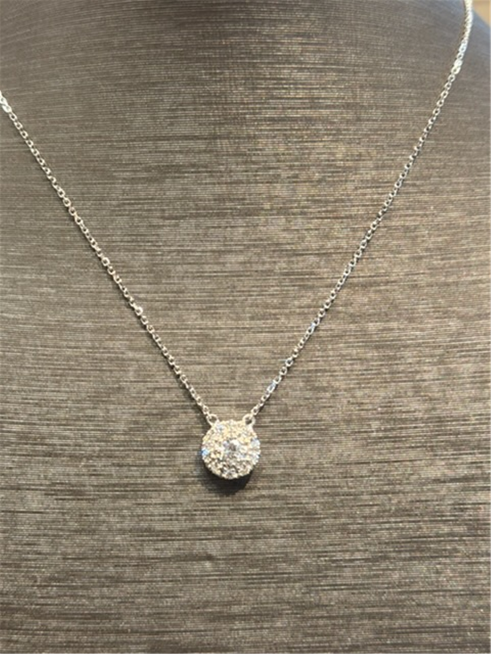 The Ryan Gems Diamond Circle Disc Pendant features a round diamond-encrusted pendant on a delicate 14k white gold chain, elegantly displayed on a gray textured bust.