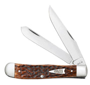 The Brown Bone Peach Seed Jig Trapper by W.R. Case & Sons Cutlery Co. features two open stainless steel blades. Its handle showcases a rugged peach seed jigged brown bone design with silver bolsters at both ends, and the word "CASE" is engraved on a metallic shield embedded in this classic Trapper's handle.