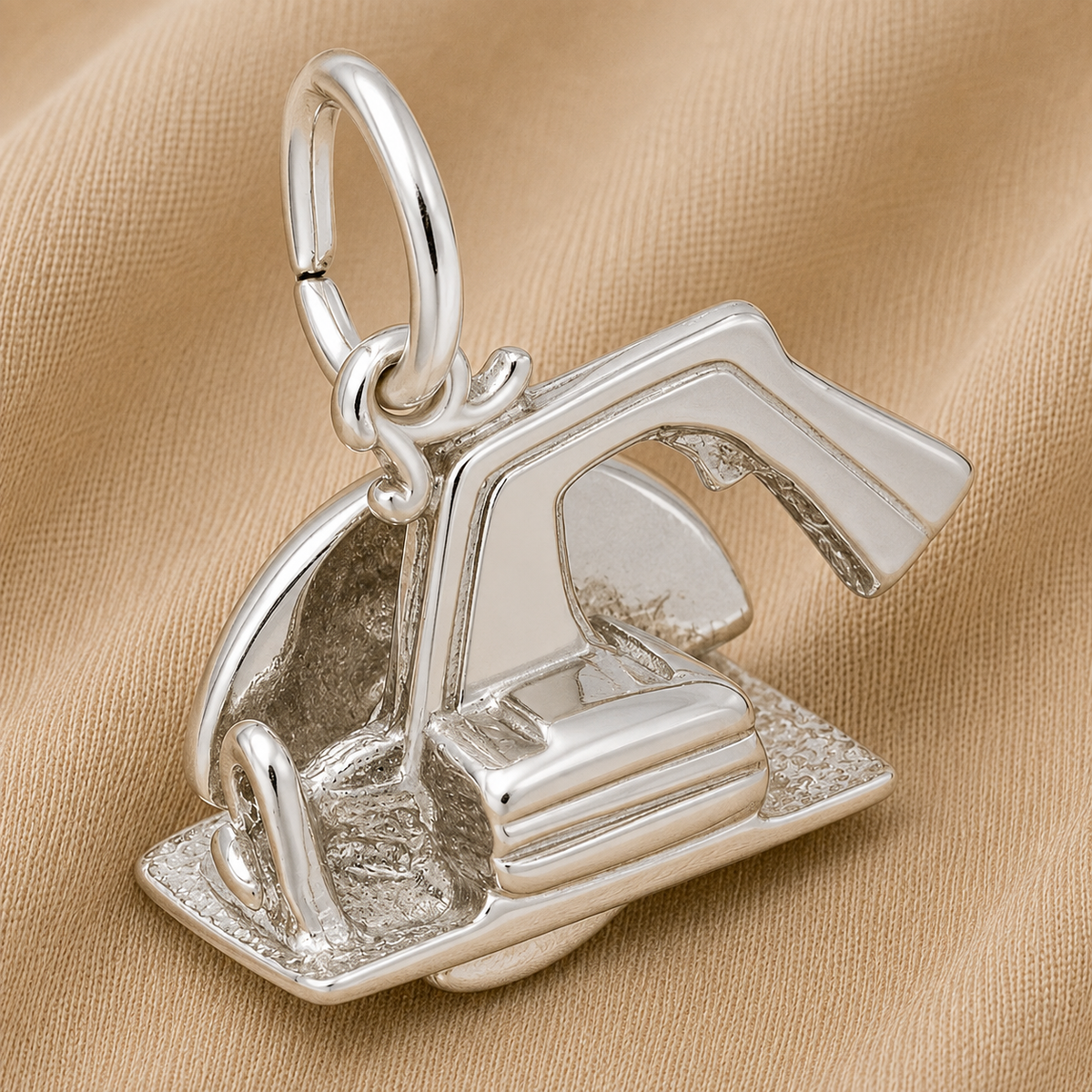 A shiny sterling silver charm shaped like an electric saw from Rembrandt Charms sits on a tan fabric background, highlighting its detailed features and craftsmanship—a perfect piece of power tool jewelry that makes a unique gift for any carpenter.