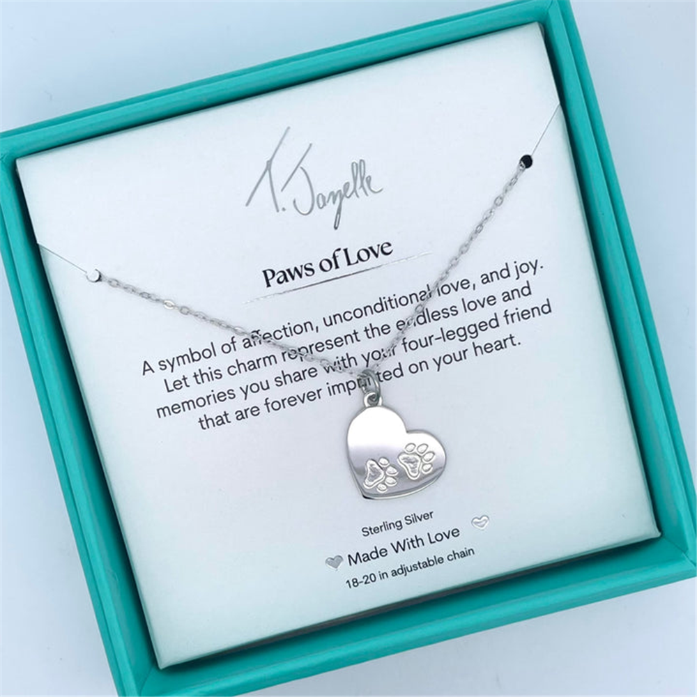 The Paws of Love Sterling Silver Charm Necklace by T Jazelle features a heart-shaped pendant engraved with paw prints, comes in a turquoise box, and includes a display card reading: “Paws of Love,” symbolizing cherished memories.