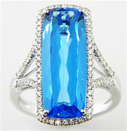 An exquisite ring from Bellarri's Silk Road Collection, the Blue Topaz and Diamond Ring D-0.40 BT-9.25 14KW S showcases a large, rectangular-cut Blue Topaz at its center, encircled by a halo of small, brilliant diamonds. The band features an intricate split design on each side, further embellished with additional small diamonds for a truly ornate finish.