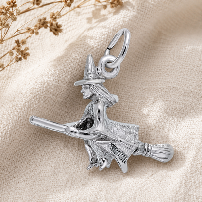 The Witch Charm- Sterling Silver by Rembrandt Charms is displayed on a beige fabric background with dried flowers in the corner—an enchanting piece of Halloween jewelry perfect for adding a touch of magic to your collection.