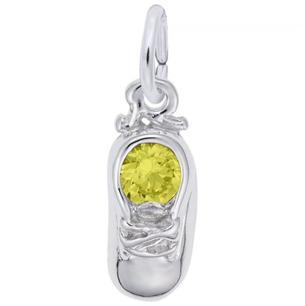 The image shows the Sterling Silver November Baby Shoe Charm from Rembrandt Charms. The charm is crafted in sterling silver and features a detailed baby shoe with a topaz-colored stone. It measures 0.2 inches by 0.43 inches (5 mm x 11 mm) and has the style number 2734-011. This charm is a perfect keepsake for commemorating the birth of a November baby.