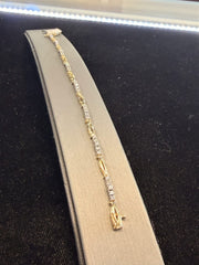 The Station Diamond and Gold Tennis Bracelet by Ryan Gems, crafted in 18k white and yellow gold, is showcased on a curved gray stand against a black background, with bright lighting accentuating its sparkling diamonds.