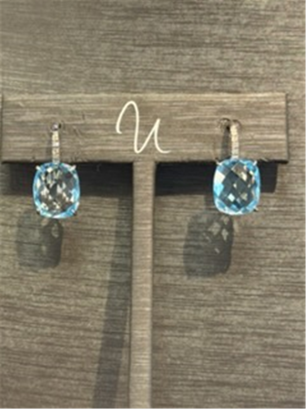 A pair of Light Blue Topaz and Diamond Drop Earrings by Ryan Gems in 14k white gold, shown on a wooden stand against a wood-textured background.