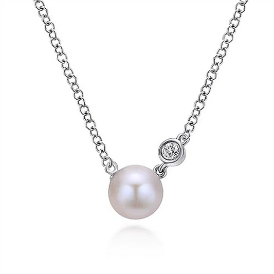 The Gabriel & Co 925 Sterling Silver Cultured Pearl and Pendant Diamond Necklace showcases a simple and elegant design featuring a single cultured pearl pendant and a small round diamond on a delicate sterling silver chain. The centered pearl, with the adjacent diamond, adds subtle sophistication to the piece.