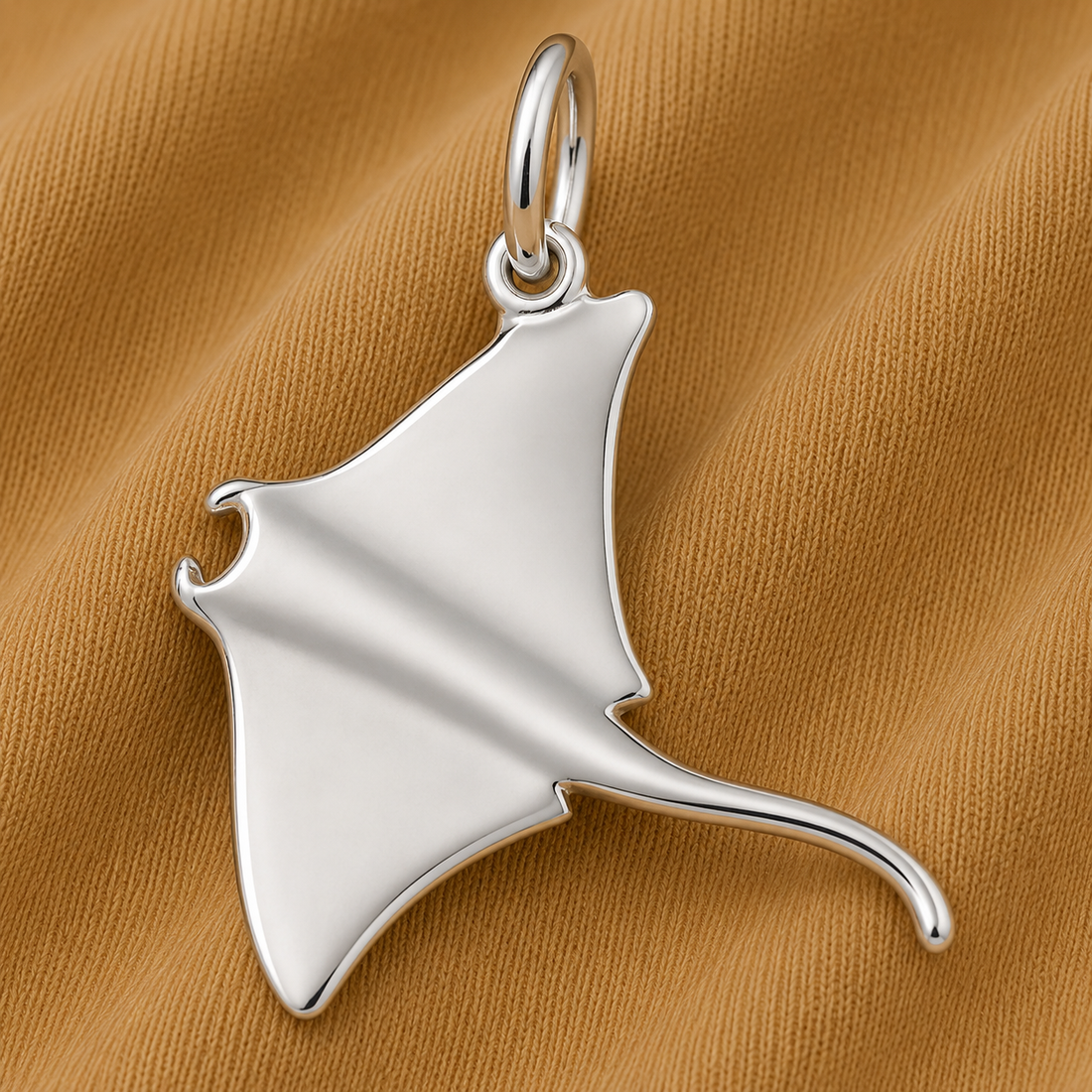 The Manta Ray Charm in sterling silver by Rembrandt Charms rests on textured brown fabric—an elegant, ocean-inspired jewelry piece that beautifully captures the graceful spirit of marine life.