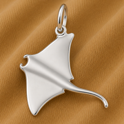 The Manta Ray Charm in sterling silver by Rembrandt Charms rests on textured brown fabric—an elegant, ocean-inspired jewelry piece that beautifully captures the graceful spirit of marine life.