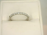 A 14K White Gold .4000ctw Round Cut Diamond Anniversary Band by Benchmark Rings is displayed on a white cushioned stand. The ring, adorned with a row of small, sparkling lab-grown diamonds set in a straight line, is showcased in a close-up, highlighting the intricate detailing and brilliance of the stones.