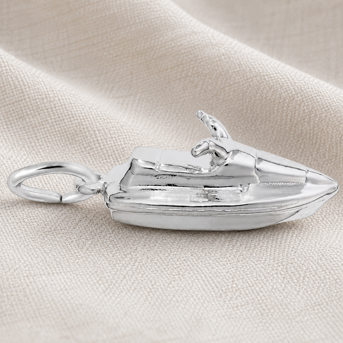 A Rembrandt Charms Jet Ski Charm in sterling silver, featuring a loop for easy attachment, is displayed on a textured beige fabric background—ideal for beach lovers and watersports enthusiasts.