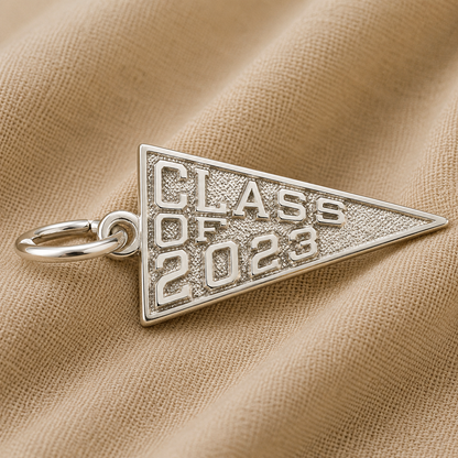 A Rembrandt Charms “Class of 2023” sterling silver charm, featuring a sleek triangular design, is elegantly displayed on beige fabric—an ideal piece of graduation jewelry to celebrate this special milestone.