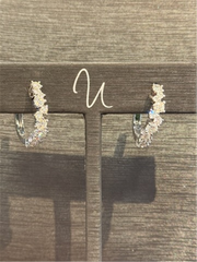 The Stagard Diamond Hoops by Ryan Gems, crafted in 14k white gold, are adorned with sparkling diamonds and displayed on a brown stand against a textured background.