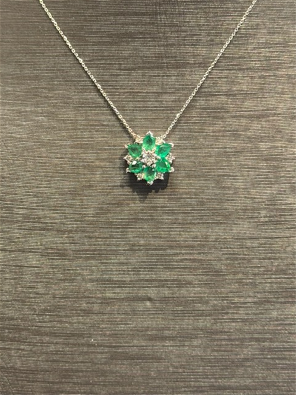 A pair of Ryan Gems Emerald Drop studs in 14k yellow gold, set with green gemstones and small clear stones, displayed on a textured brown background.