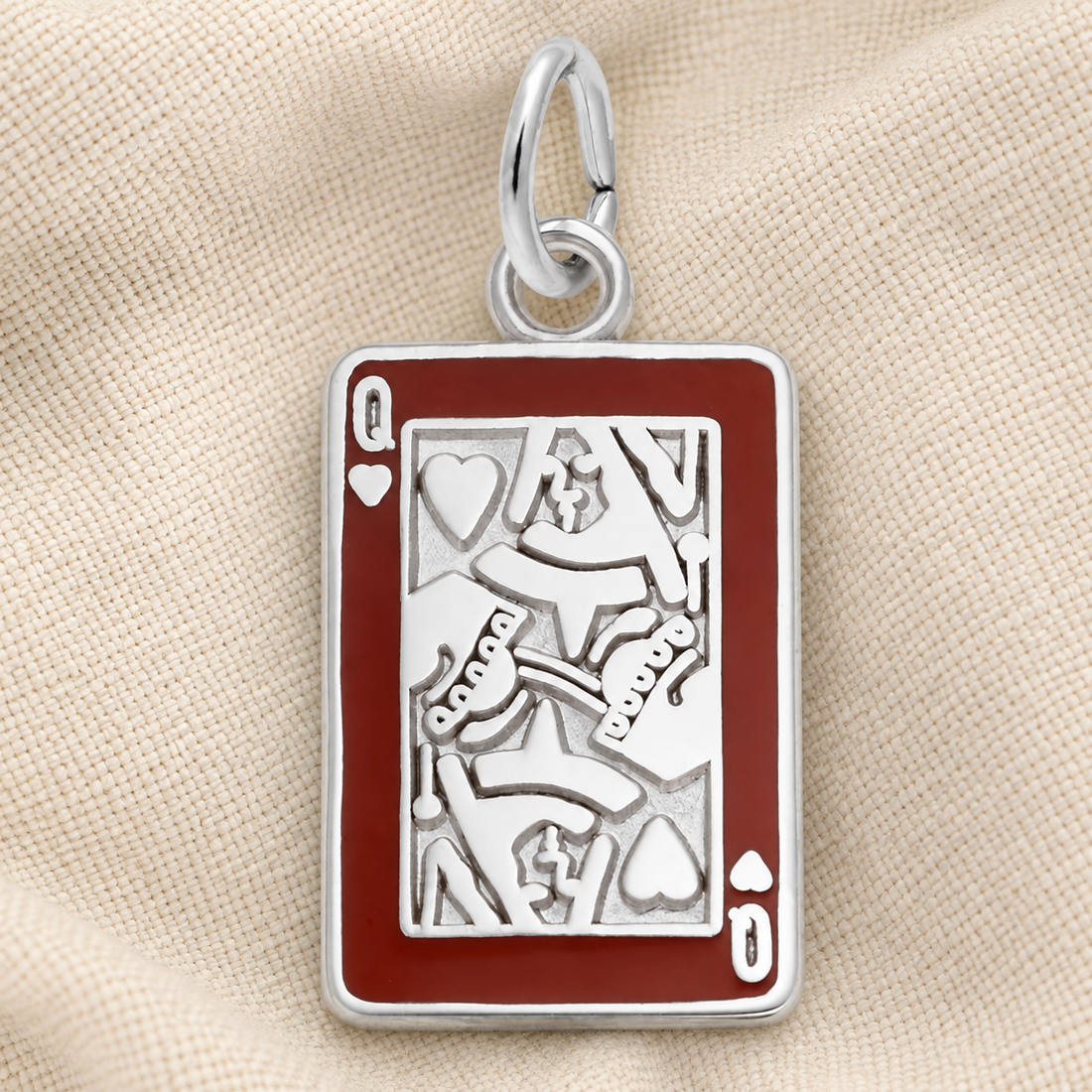 The Rembrandt Charms Queen of Hearts Charm—crafted in sterling silver and featuring cutout details with a red border, designed in the shape of a Queen of Hearts playing card—rests on a beige fabric background.