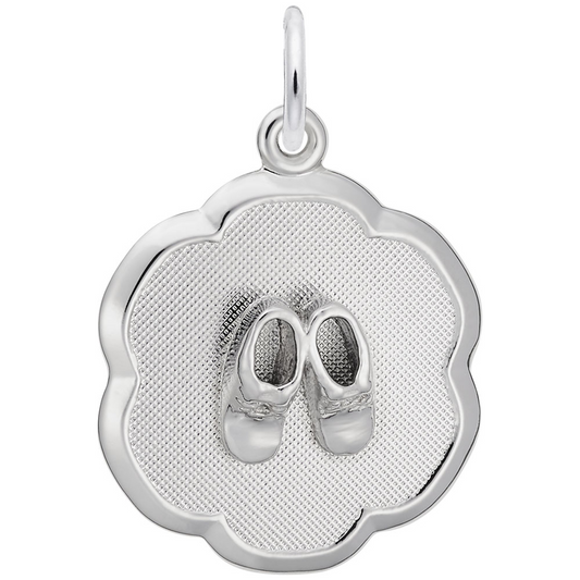 The image shows the Sterling Silver Baby Booties on Scalloped Disc Charm from Rembrandt Charms. The charm is crafted in sterling silver and features a pair of detailed baby booties set on a scalloped disc. It measures 0.69 inches by 0.69 inches (17.6 mm x 17.6 mm) and has the style number 0945. This charm is a perfect keepsake for commemorating a baby's early days.
