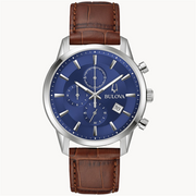The Bulova Watch Company's 6 Hand Men's Sutton Watch features an analog display with a stainless-steel case, a blue dial, and a brown crocodile leather grain strap. It includes three subdials, a date window at 4 o'clock, silver hour markers, and luminescent hands. This watch boasts a classic, elegant design.