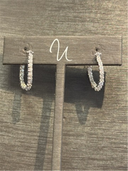 Ryan Gems' Inside Out Diamond Hoops, crafted in elegant 18k white gold, are small and sparkling, displayed on a wooden stand featuring a cursive "u" on the top bar for timeless appeal.