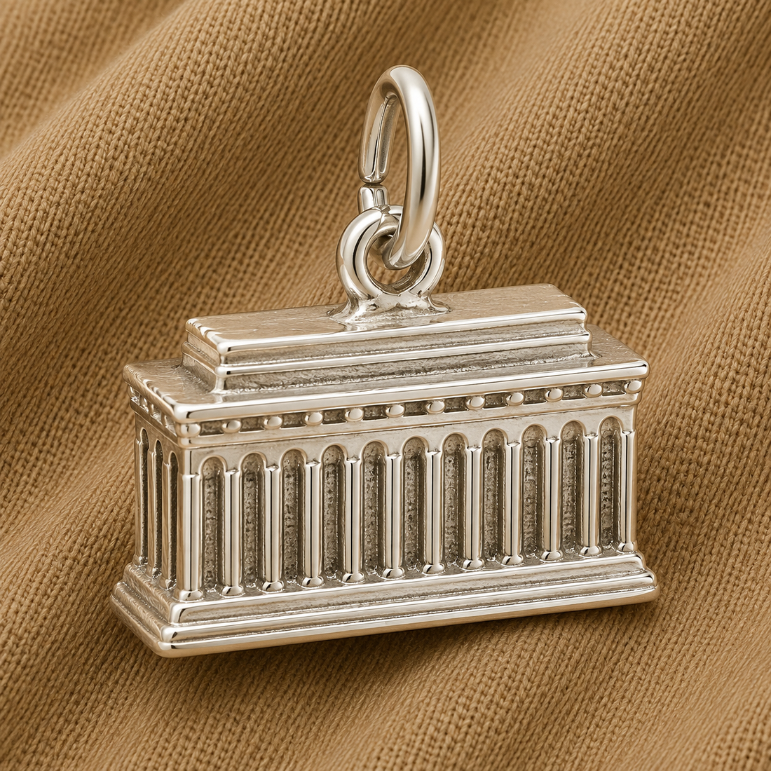 Showcased on a textured tan fabric background, the Rembrandt Charms Lincoln Memorial Charm—crafted in sterling silver—features a detailed classical design with columns, making it an elegant accessory for American history enthusiasts or a distinctive Washington DC souvenir.