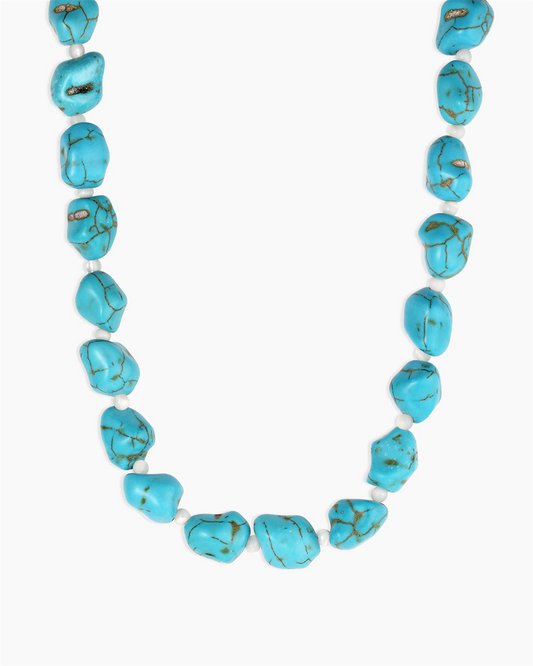 The Gorjana Turquoise Cove Necklace features irregular turquoise stones separated by small white beads, shown up close against a plain white background.