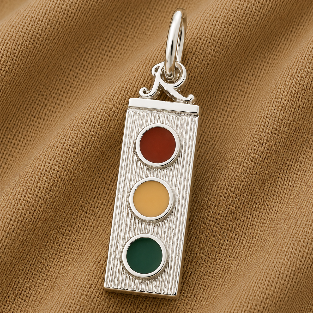 The Traffic Light Charm - Sterling Silver by Rembrandt Charms features a vertical traffic light design with red, yellow, and green circular accents. Displayed on textured brown fabric, this distinctive piece of transportation jewelry adds a subtle urban touch to any outfit.