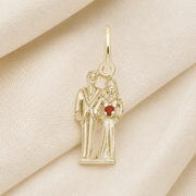The Rembrandt Charms Bride and Groom - 14K Charm features a beautifully crafted gold pendant depicting a bride and groom standing together, with the bride holding a small red bouquet accented by a delicate red bead. Photographed against a cream fabric background, this elegant charm makes for an exquisite wedding keepsake or thoughtful gift for newlyweds.