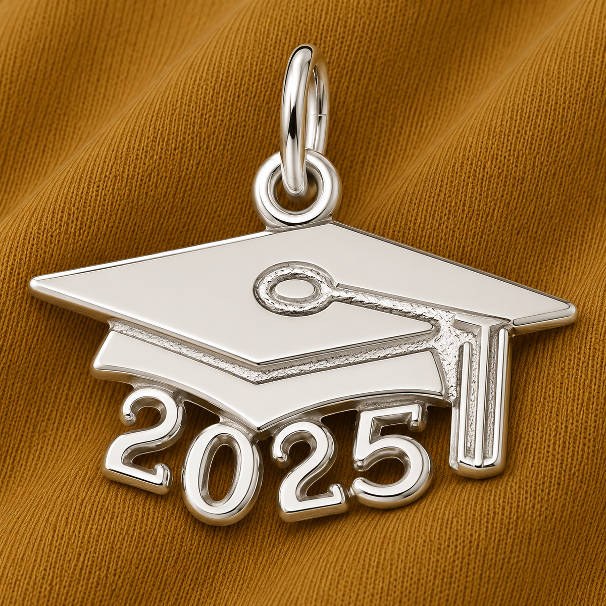 The Rembrandt Charms 2025 Grad Cap Charm in sterling silver, a thoughtful graduation gift, is elegantly displayed on a brown fabric background.