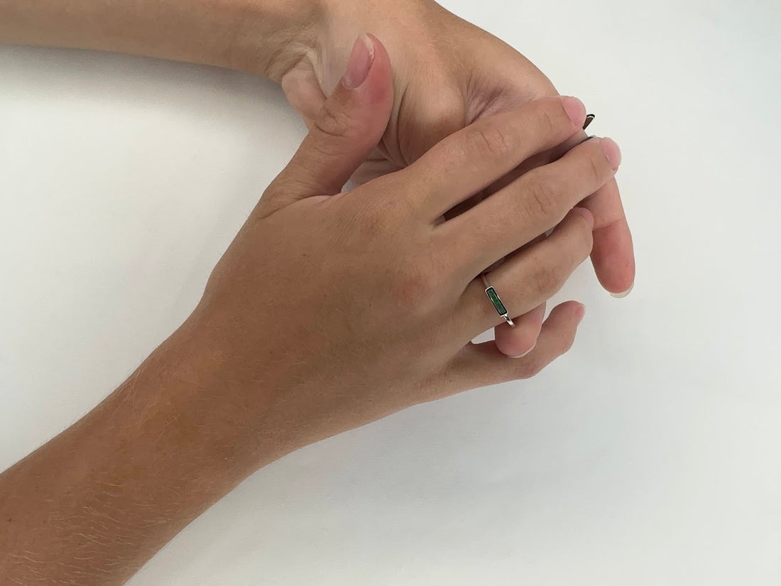 Close-up of two hands with interlocking fingers. One hand features an elegant Allison Kaufman Emeralds 14K White Gold Ring on the ring finger. The background is plain white.