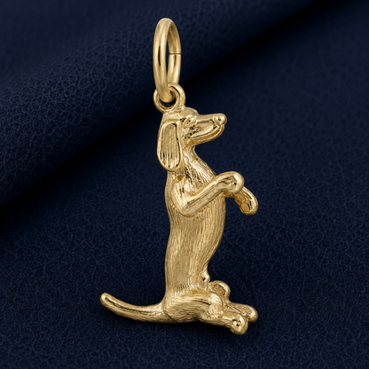 A Sitting Dachshund Charm in sterling silver by Rembrandt Charms, featuring detailed fur texture and crafted in the shape of a dog sitting upright on its hind legs, displayed against a dark blue textured background.