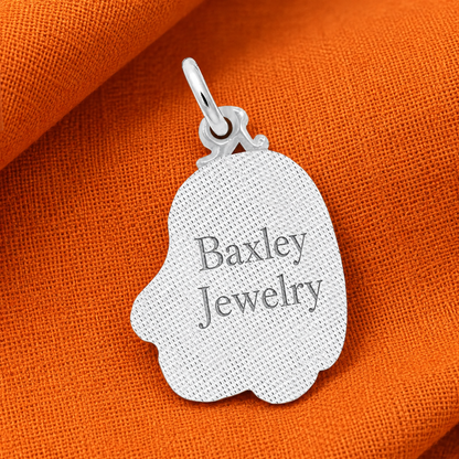 A sterling silver pendant engraved with “Baxley Jewelry” rests on orange textured fabric, accented by Rembrandt Charms’ Painted Cute Ghost Charm—an adorable Halloween accessory.
