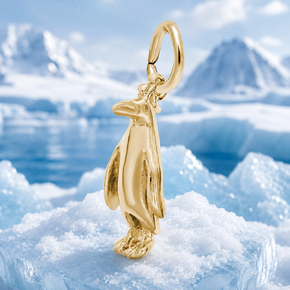 A three-dimensional Rembrandt Charms Adélie Penguin - Gold Plated Charm rests on a block of ice, with snowy mountains and a frozen lake in the background.