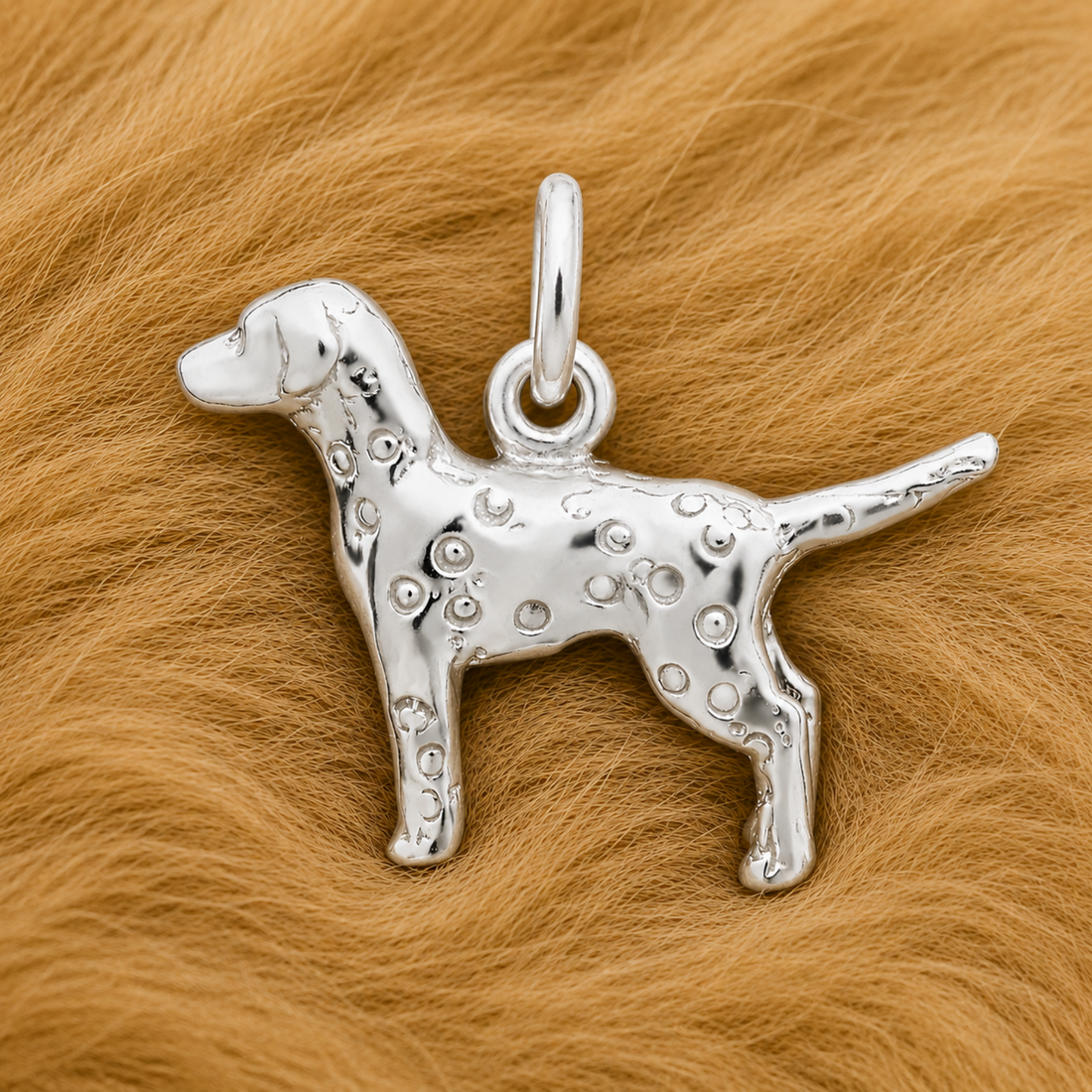 A Rembrandt Charms Dalmatian Dog Charm in sterling silver, featuring etched spots, rests on a soft, light brown, fur-like surface.