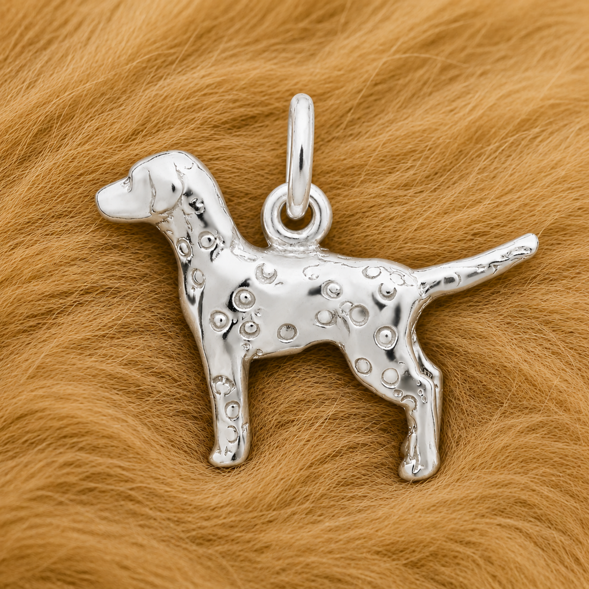 A Rembrandt Charms Dalmatian Dog Charm in sterling silver, featuring etched spots, rests on a soft, light brown, fur-like surface.