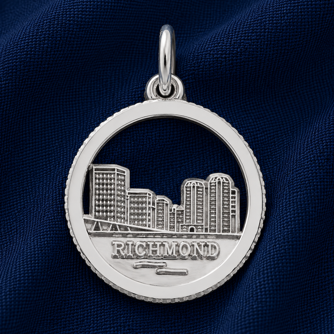 A sterling silver Kansas City skyline charm by Rembrandt Charms, featuring a cutout cityscape with “KANSAS CITY” engraved below, displayed on textured dark blue fabric—an ideal travel keepsake or a distinctive addition to your charm bracelet.