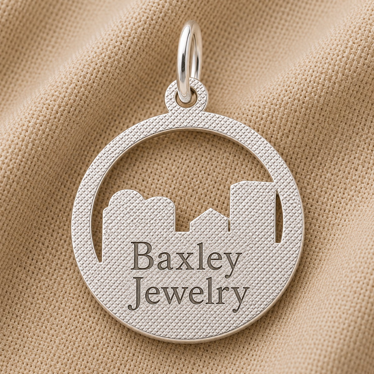 A sterling silver Kansas City Skyline Charm by Rembrandt Charms rests on beige textured fabric, making it a perfect travel keepsake or addition to your charm bracelet.