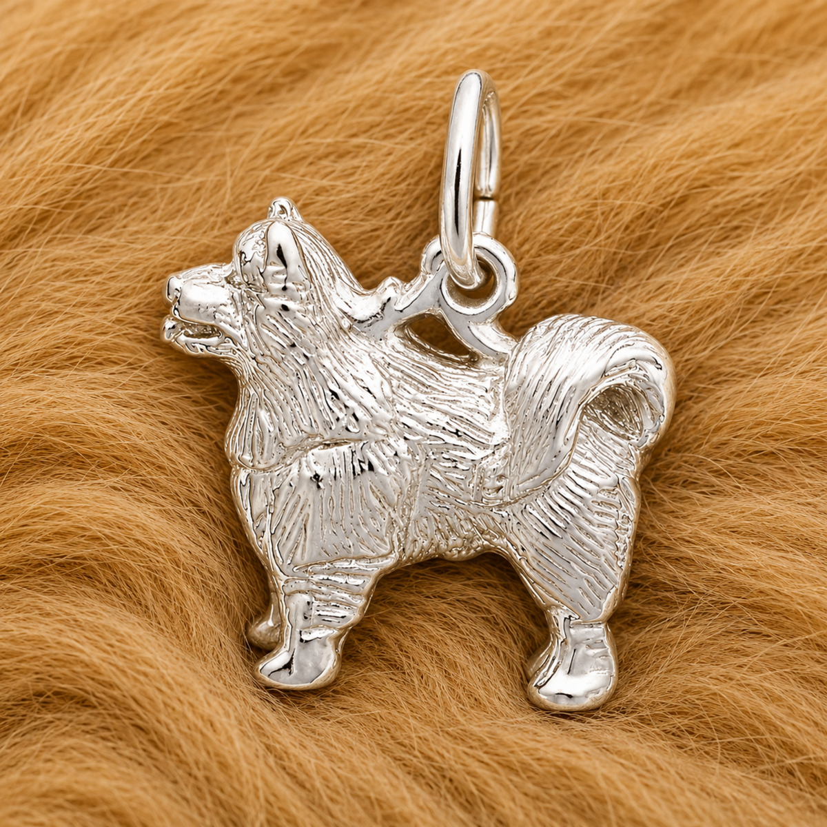 A shimmering Samoyed Dog Charm- Sterling Silver by Rembrandt Charms, inspired by a fluffy breed, rests gracefully on a soft, light brown furry surface—an ideal jewelry piece for dog lovers. This elegant sterling silver charm perfectly embodies the spirit of the beloved Samoyed and adds sophisticated charm to any collection.