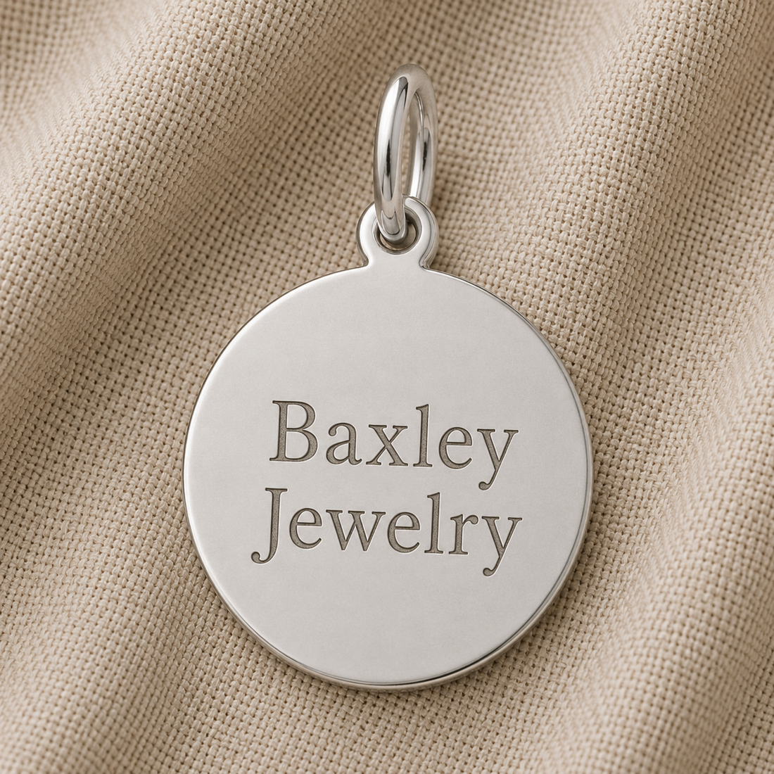 A round sterling silver Medium Diamond Faceted Disc Charm by Rembrandt Charms rests on beige textured fabric, making it a timeless piece of personalized jewelry.
